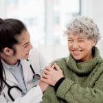 woman doctor and woman patient smiling together in office. Small microphone icon in white circle in top right circle of the photo.